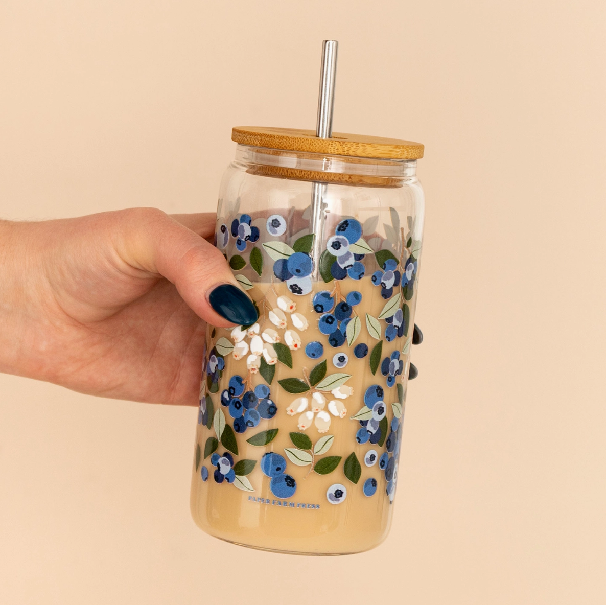 Hand holding a floral-patterned tumbler with a bamboo lid and metal straw on a beige background