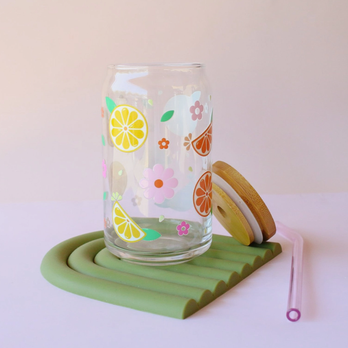 Glass tumbler with lemon and flower design on a green coaster with a pink straw.