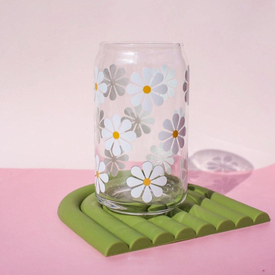 Clear glass with floral design on a green coaster against a pink background