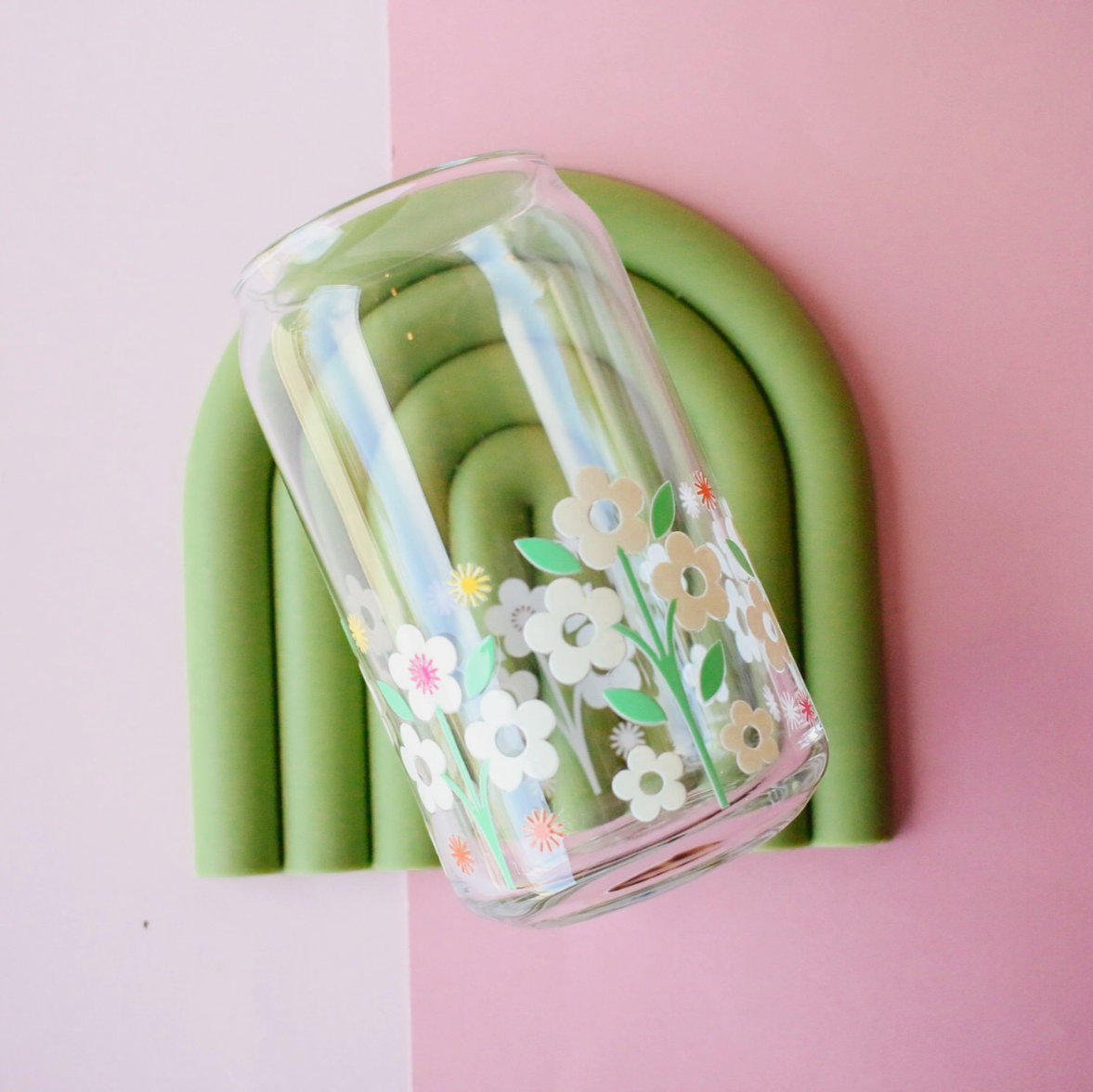 Glass with floral design and straw on a green coaster against a pink background