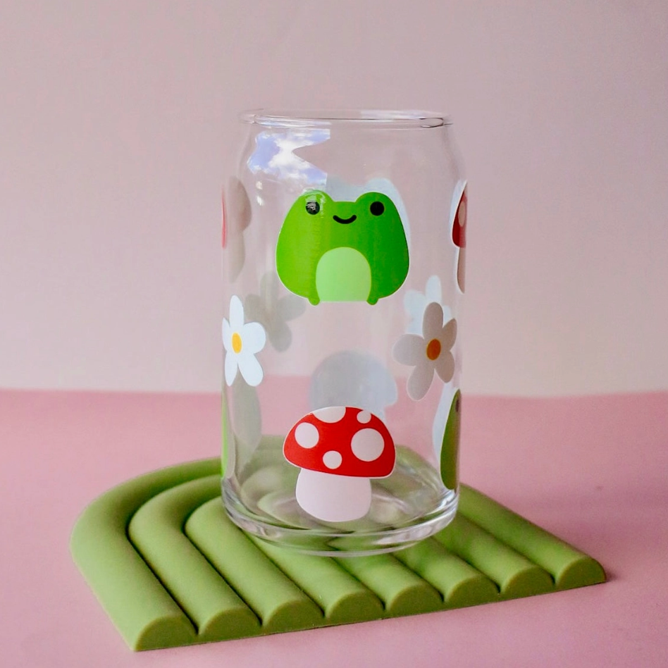Glass with a green frog and red mushroom design on a pink background