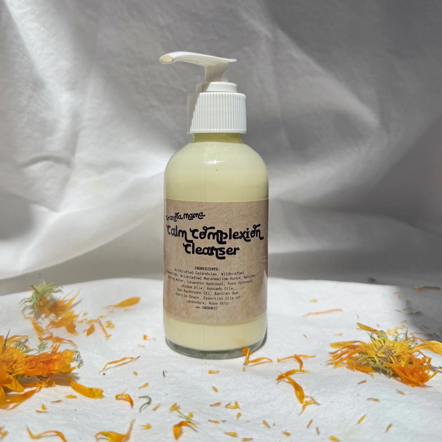 Bottle of 'Calm Complexion Cleanser' with pump on a white background with orange flowers.