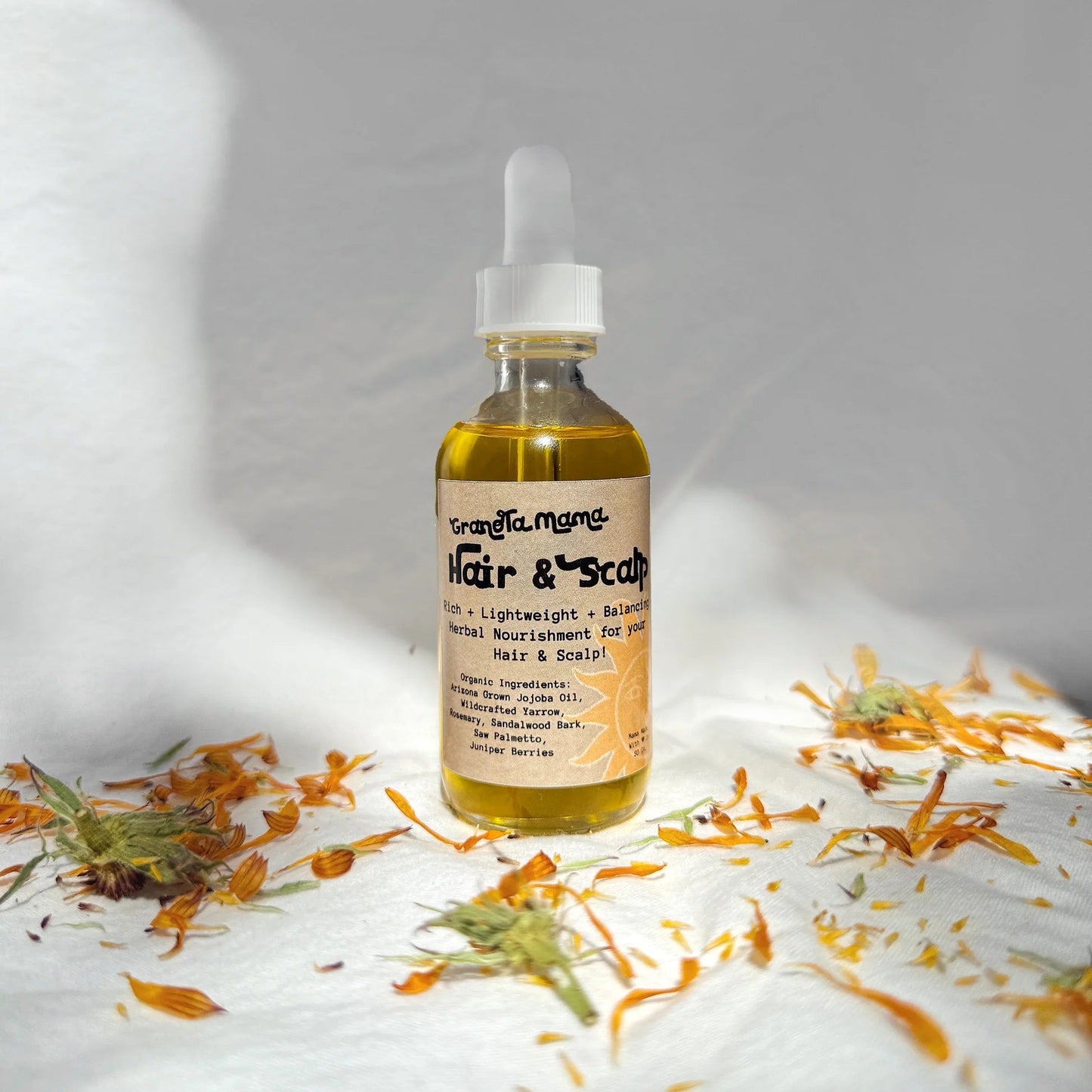 Bottle of hair and scalp oil with flowers on a white surface