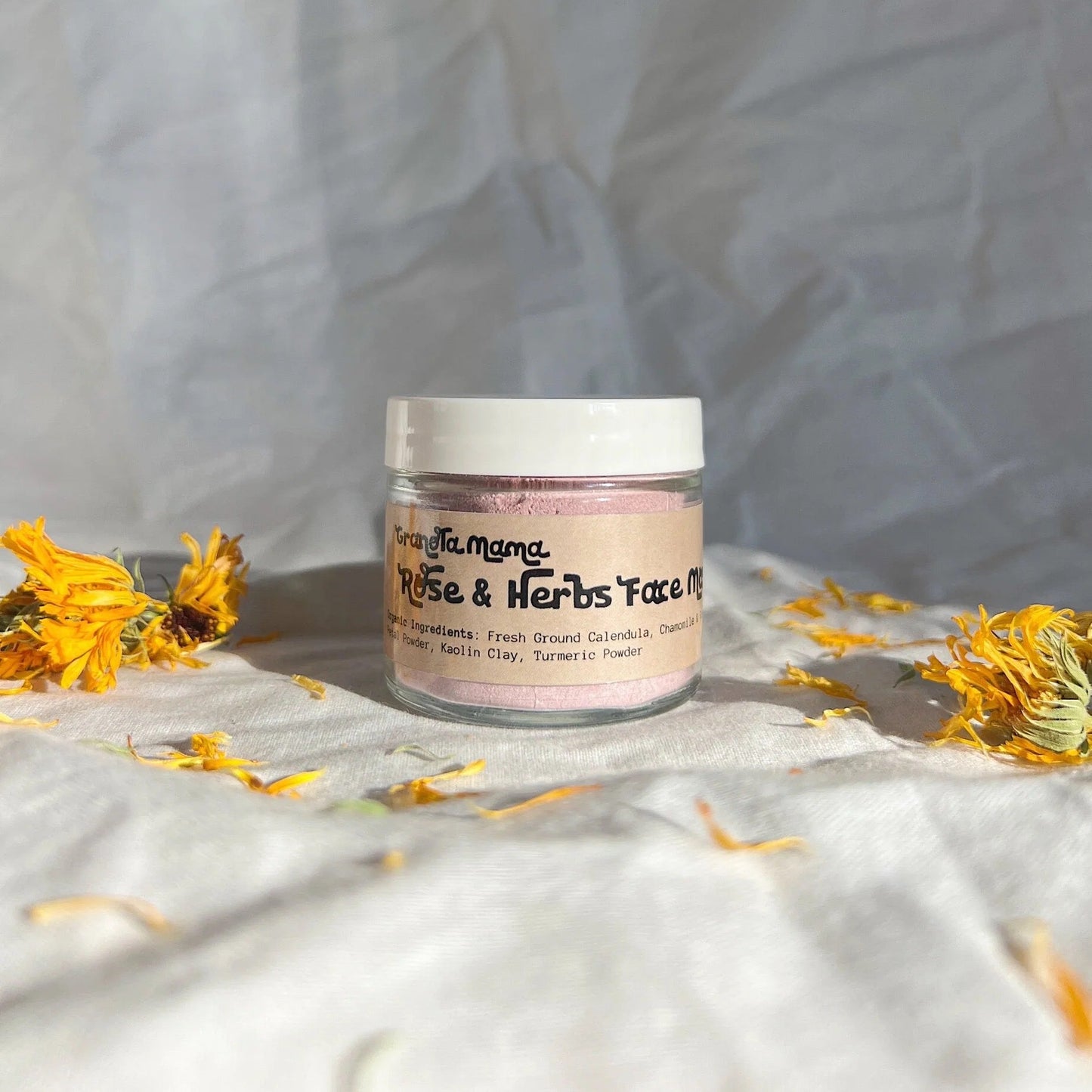 Jar of face mask with dried flowers on a textured fabric background