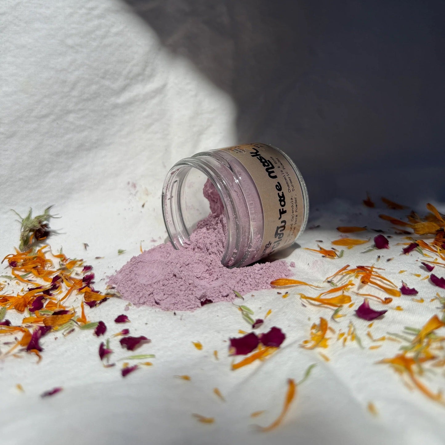 Small jar of pink face mask powder with dried flowers on a white surface