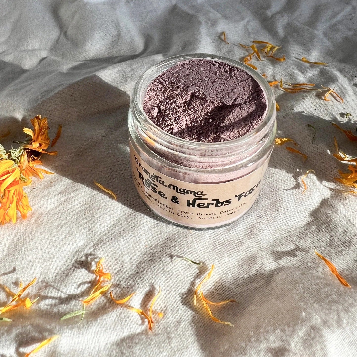 Jar of pink face powder with dried flowers on a textured surface