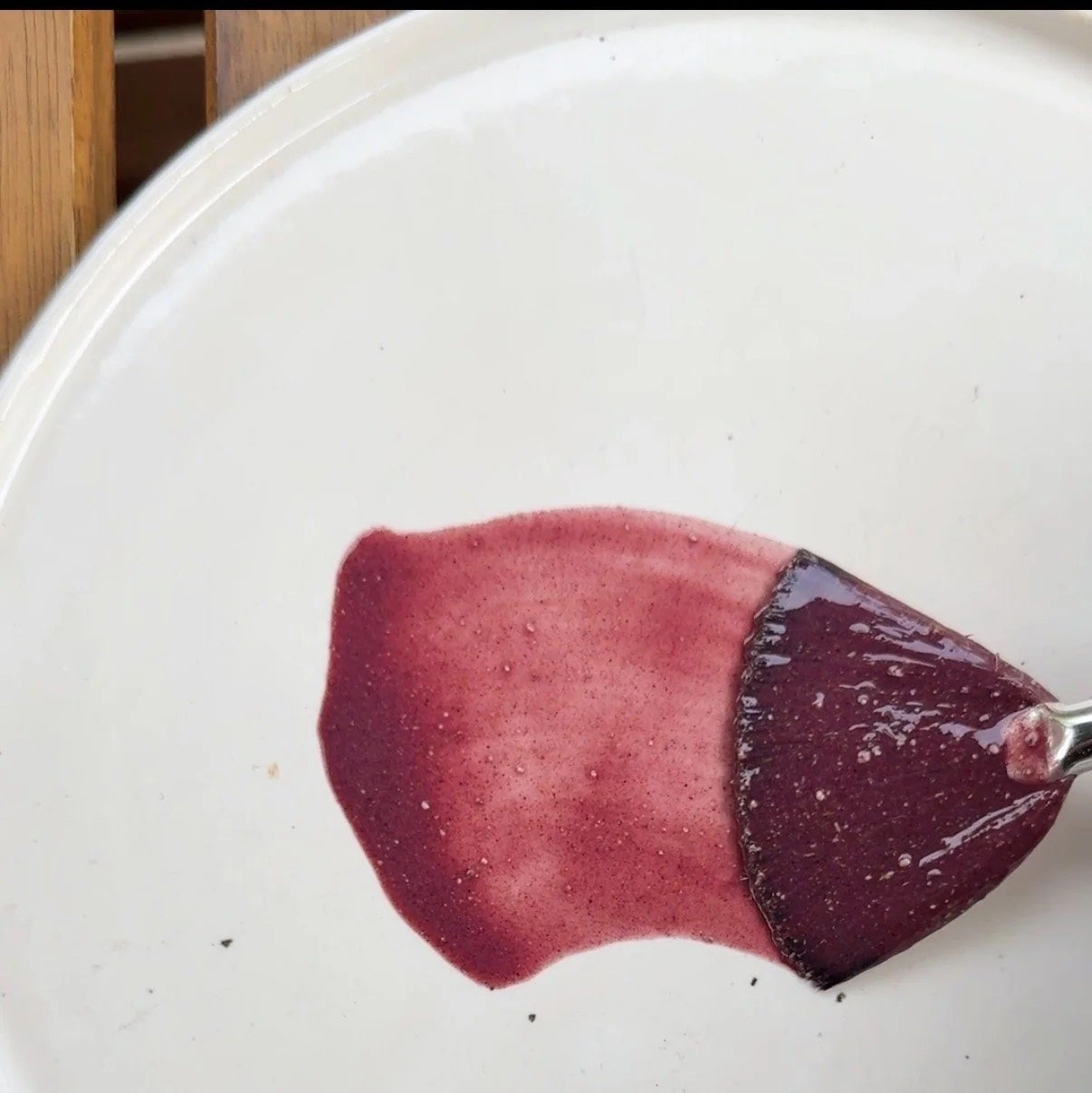 Purple face mask mixes with water on a white plate with a wooden surface underneath