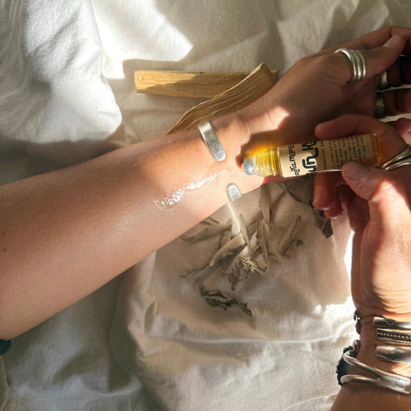 Person applying a granola mama essence from a tube onto wrist, with a white cloth in the background.