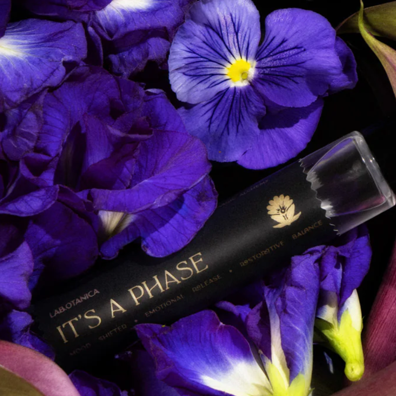 Perfume 'It's a Phase' branding surrounded by purple and pink flowers on a dark background