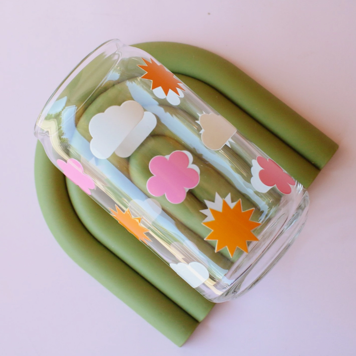Drinking glass with cloud flower and sun stickers on a light pink background