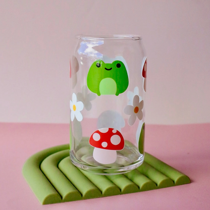 Glass with a green frog and red mushroom design on a pink background