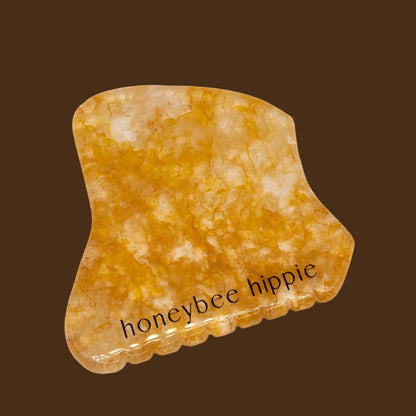 Yellow gua sha stone with 'honeybee hippie' text on a beige background