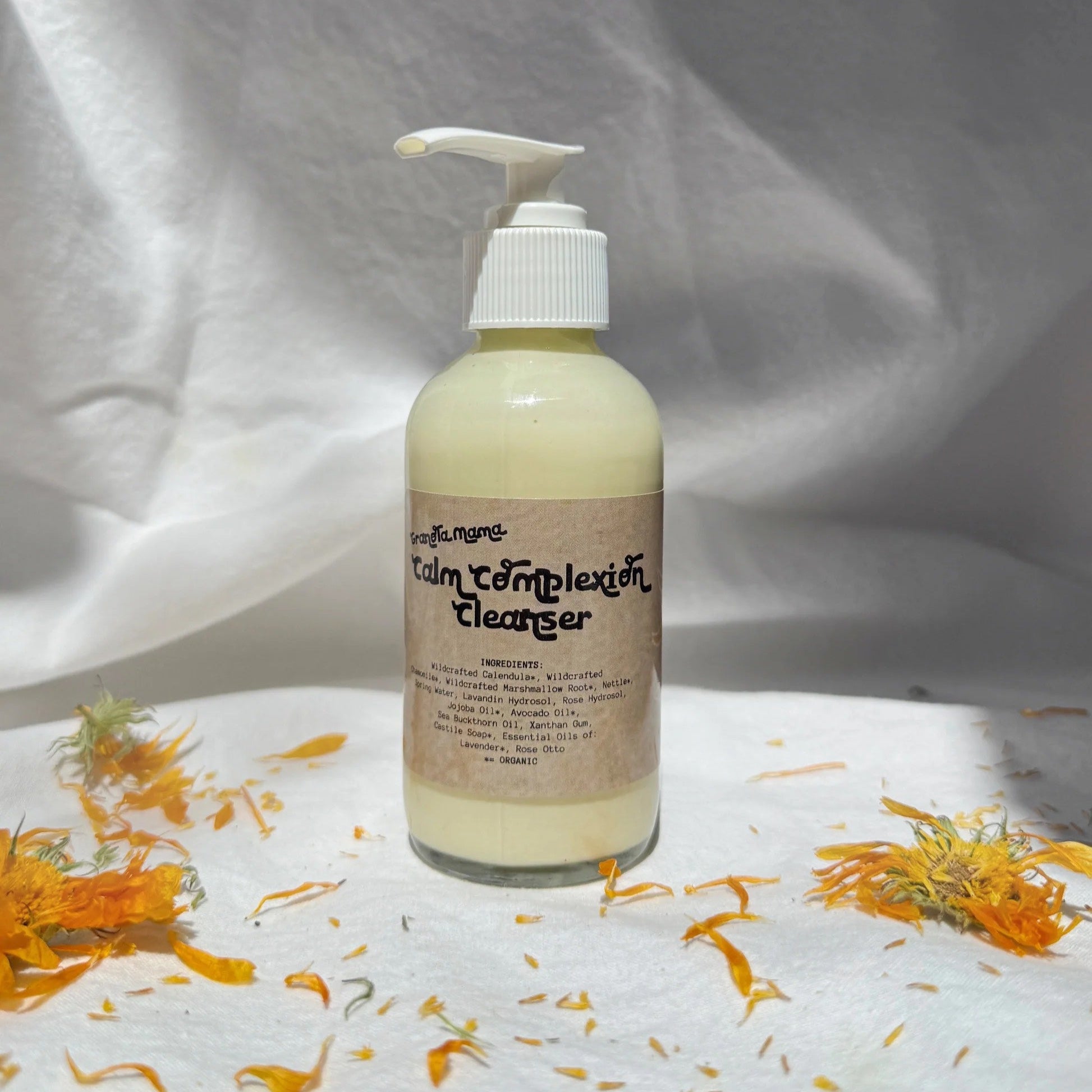 Bottle of 'Calm Complexion Cleanser' with pump on a white background with orange flowers.
