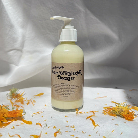 Bottle of 'Calm Complexion Cleanser' with pump on a white background with orange flowers.