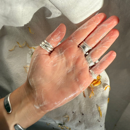 Hand with rings on a white fabric background showing cleanser on hand. 