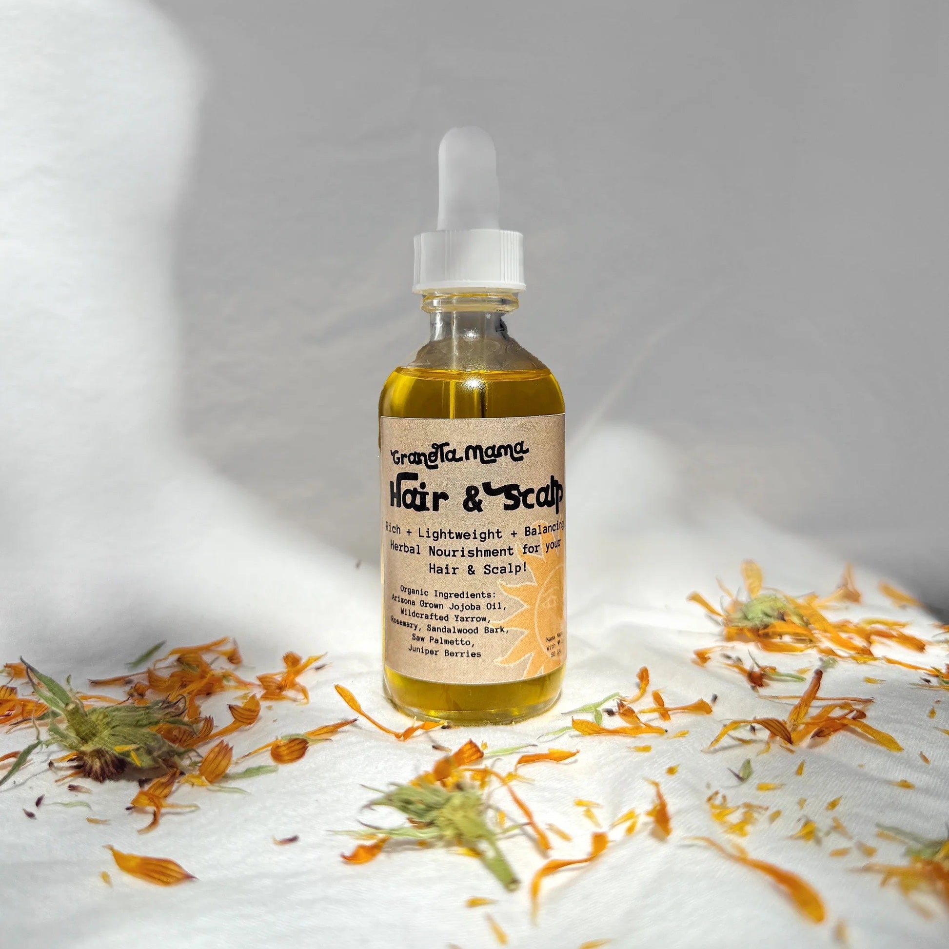 Bottle of hair and scalp oil with flowers on a white surface