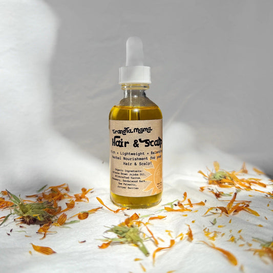 Bottle of hair and scalp oil with flowers on a white surface