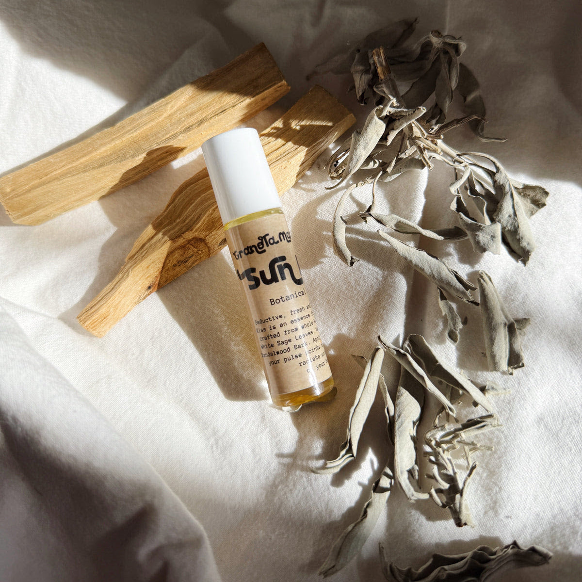 Small bottle with a white cap on a light fabric background with dried herbs and wooden sticks.