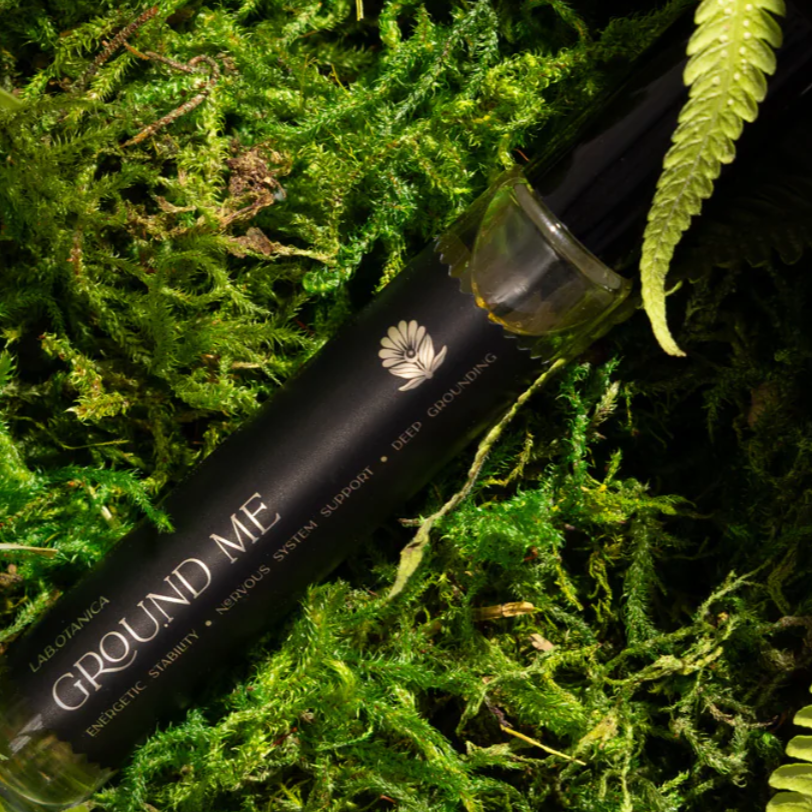 Ground Me Perfume on green moss with a dark background