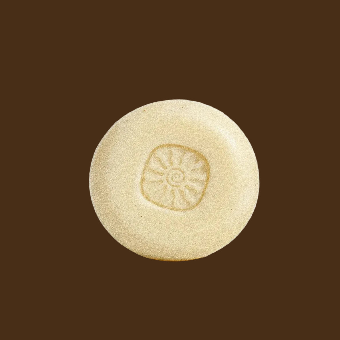 A single round, pale cream-colored soap bar with a sunburst pattern embossed in the center, photographed on a clean white background.