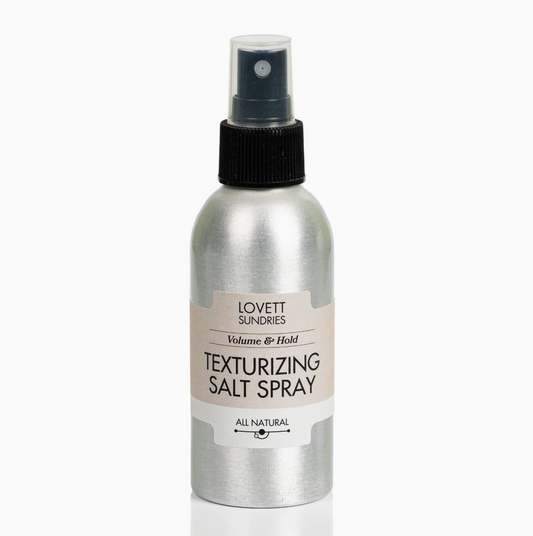 A silver aluminum spray bottle of Lovett Sundries Texturizing Salt Spray with a black spray nozzle and a beige label, set against a plain white background.