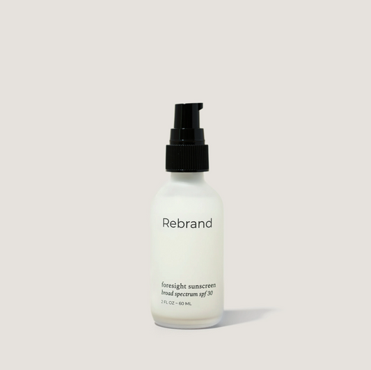Sunscreen bottle labeled 'Rebrand' on a light gray background