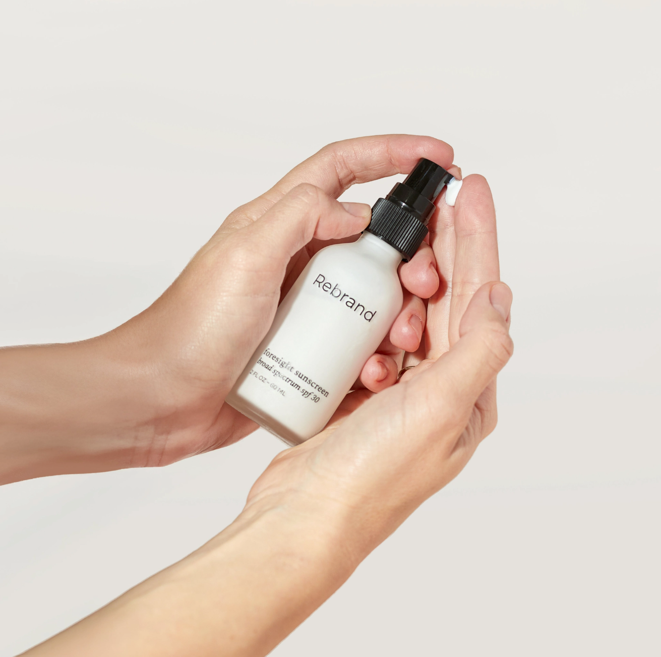 Person holding a bottle labeled 'Rebrand' against a plain background